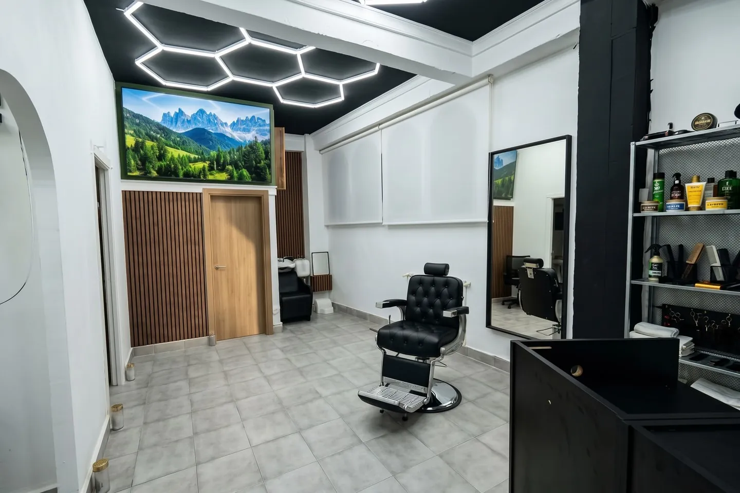 Zona de barbería: sillón de barbero frente al espejo, con la estantería de productos y las luces hexagonales del techo